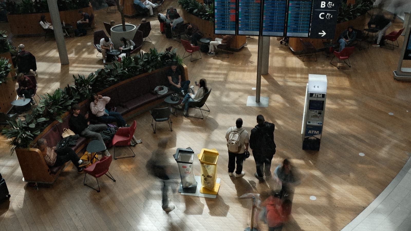 Travelers waiting below a departure board inside a real airport terminal