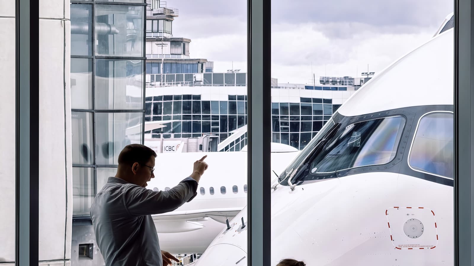 Father and daughter watching an aircraft through an airport gate window