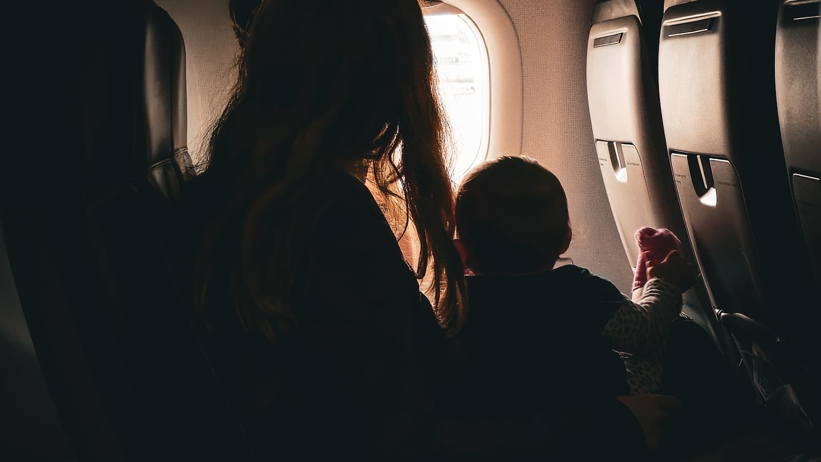 Mother holding a baby while looking through an airplane window