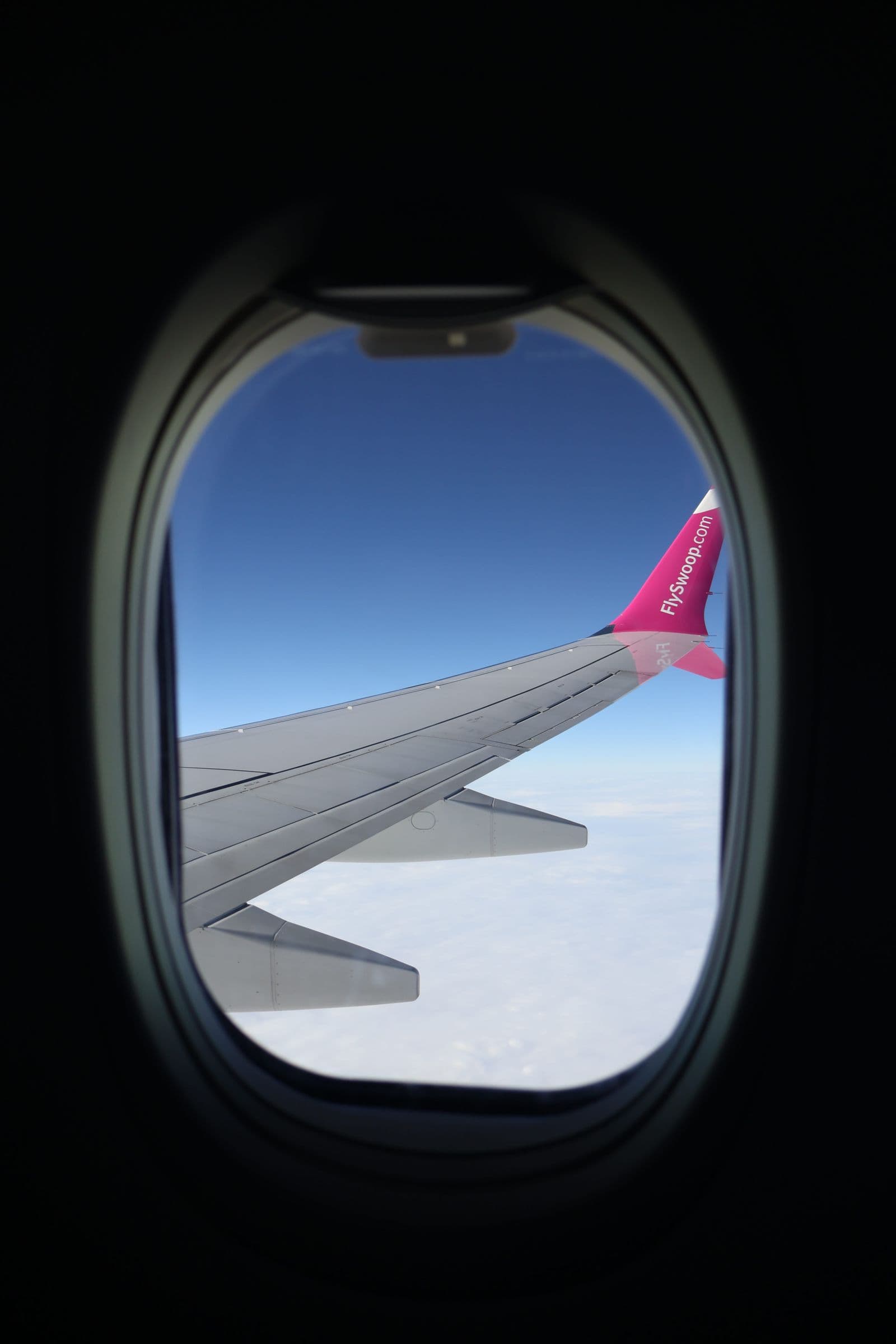 Unbranded airplane wing above a bright blue sky