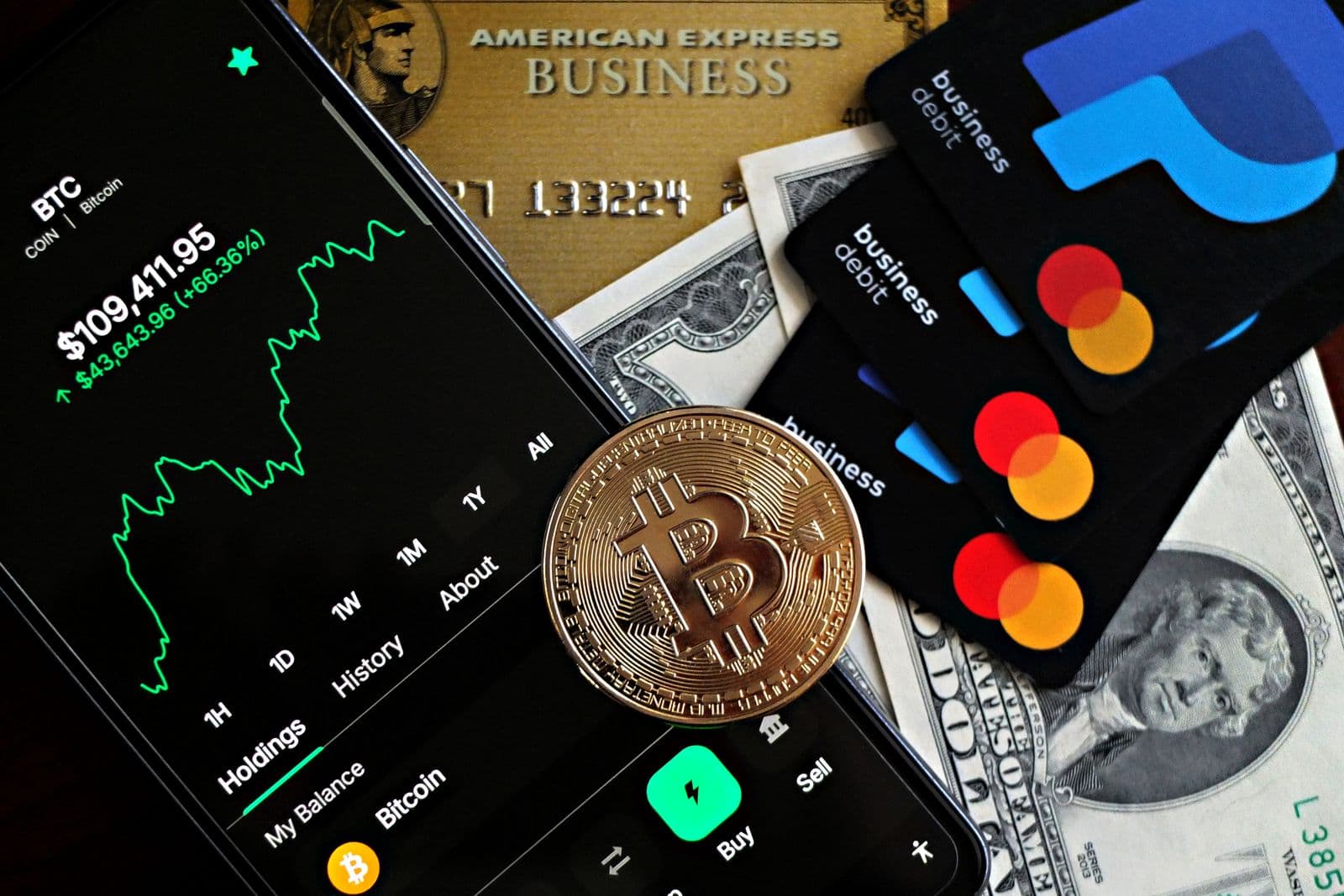 Phone displaying a cryptocurrency chart beside cards and a Bitcoin coin