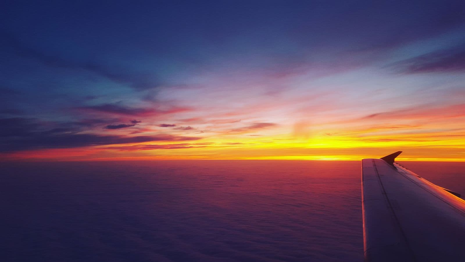Unbranded airplane wing framed against a colorful sunset sky