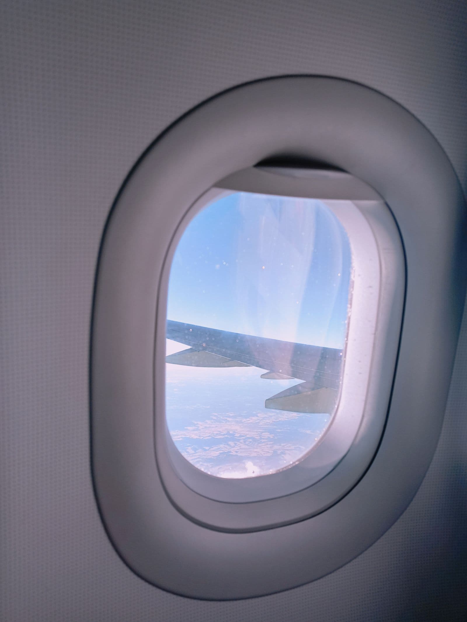 Airplane wing and clouds viewed through a passenger window