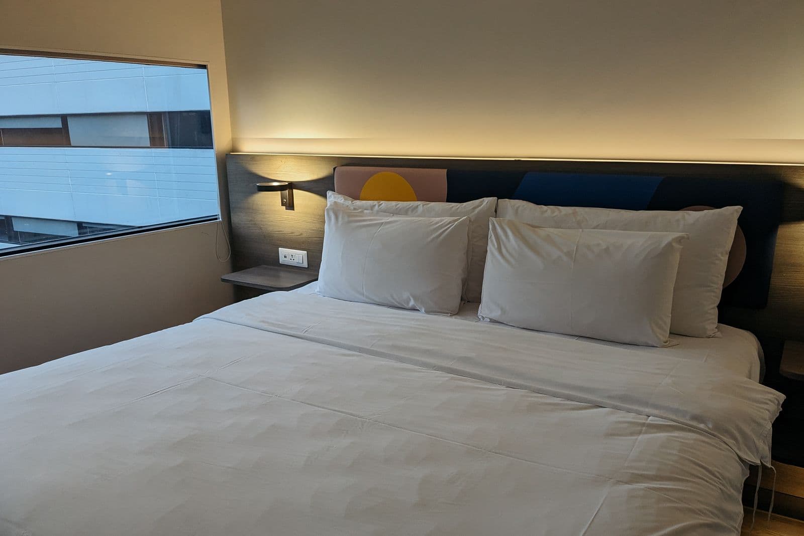 Hotel bedroom with white bedding and a window overlooking a nearby building