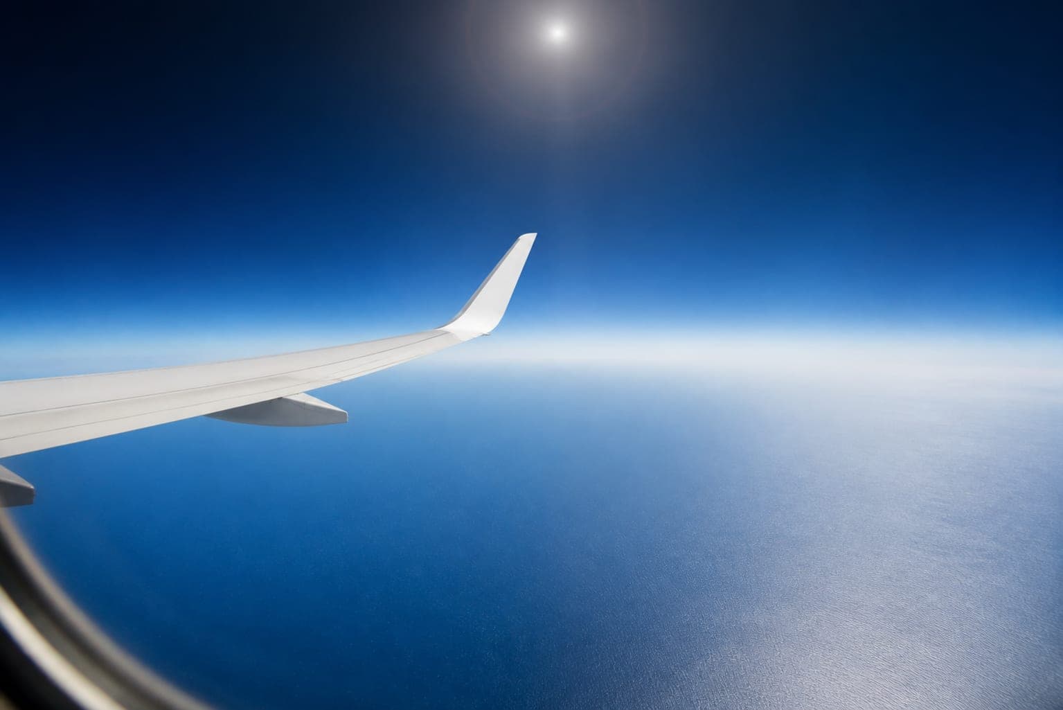 Airplane winglet high above open ocean with a sun halo