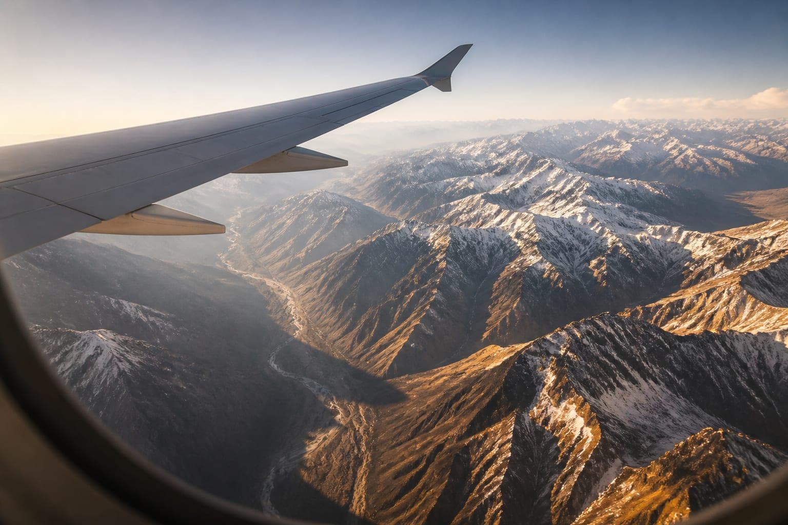 Airplane wing over snow-dusted Andes ridgelines in golden light