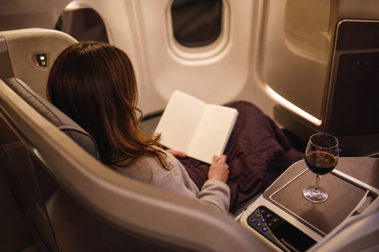 Traveler reading in a lie-flat business class seat with a glass of wine