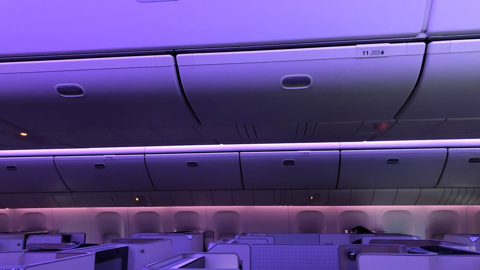 Real passenger cabin with rows of aircraft seats under purple lighting