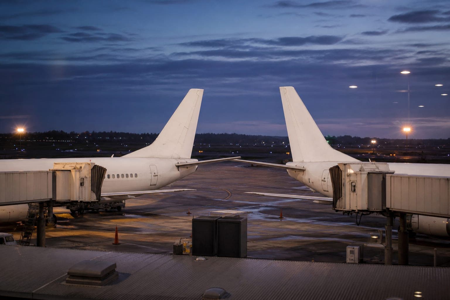 Two unbranded white aircraft tails at adjacent gates at dusk